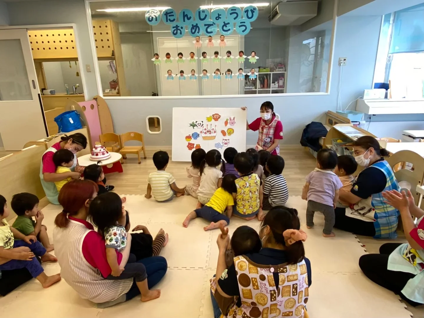 園のお誕生日会。子どもたちのそばで保育者が見守っています。