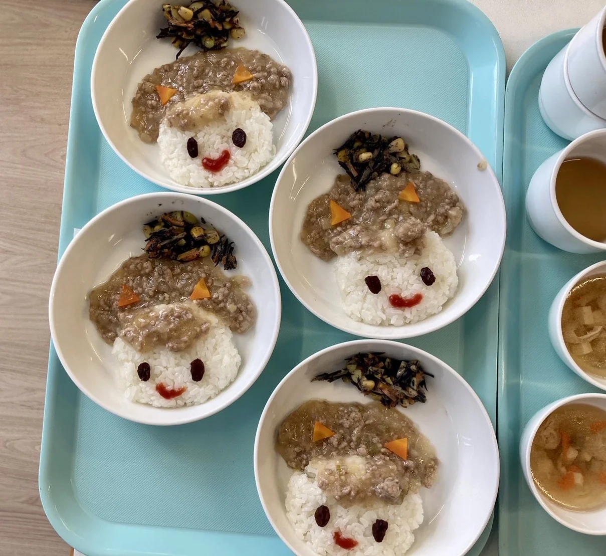 顔の形に盛り付けられたごはんとおかず、汁物の給食。