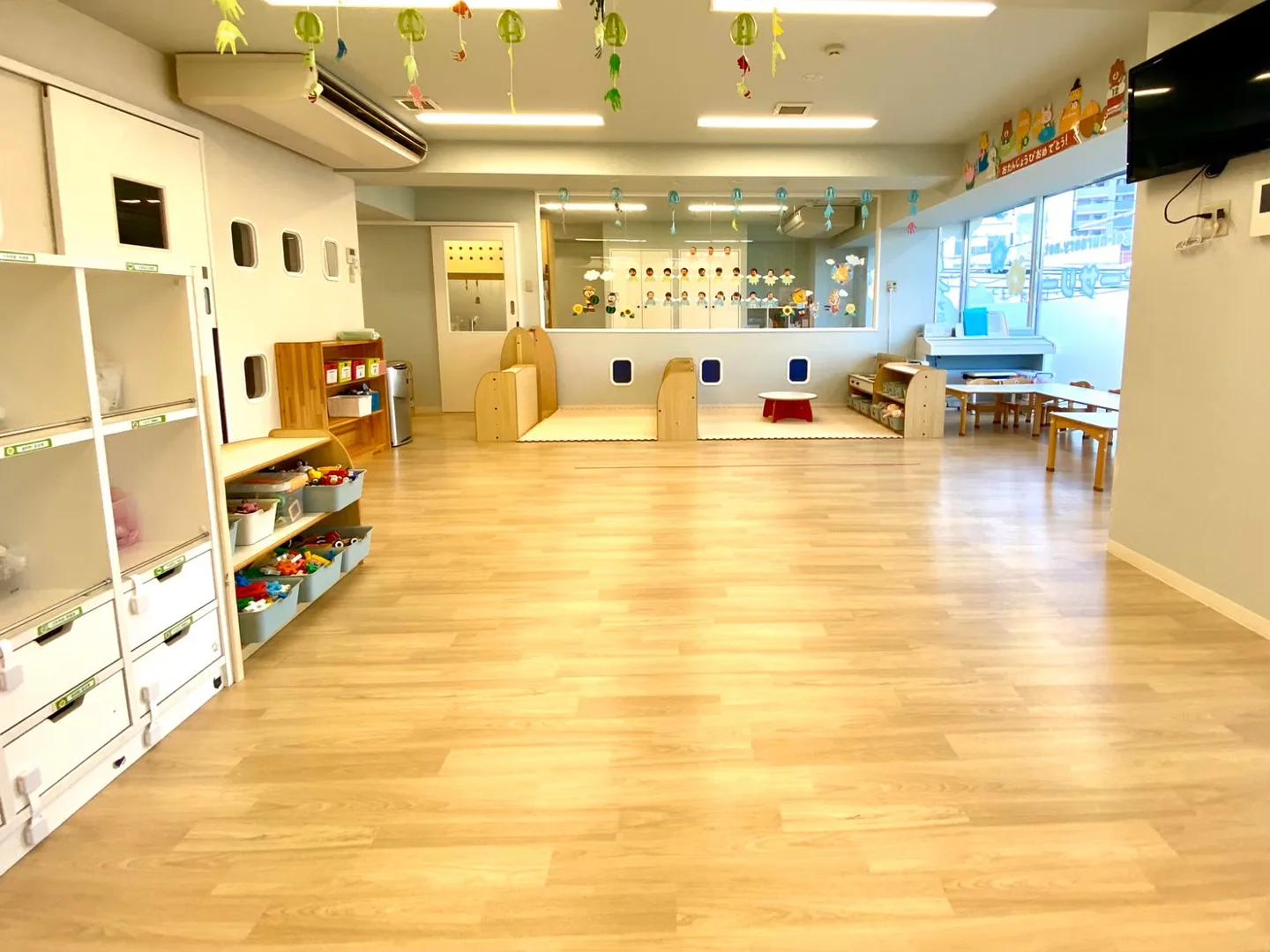 木目の床と木製の家具がある保育室の全景。